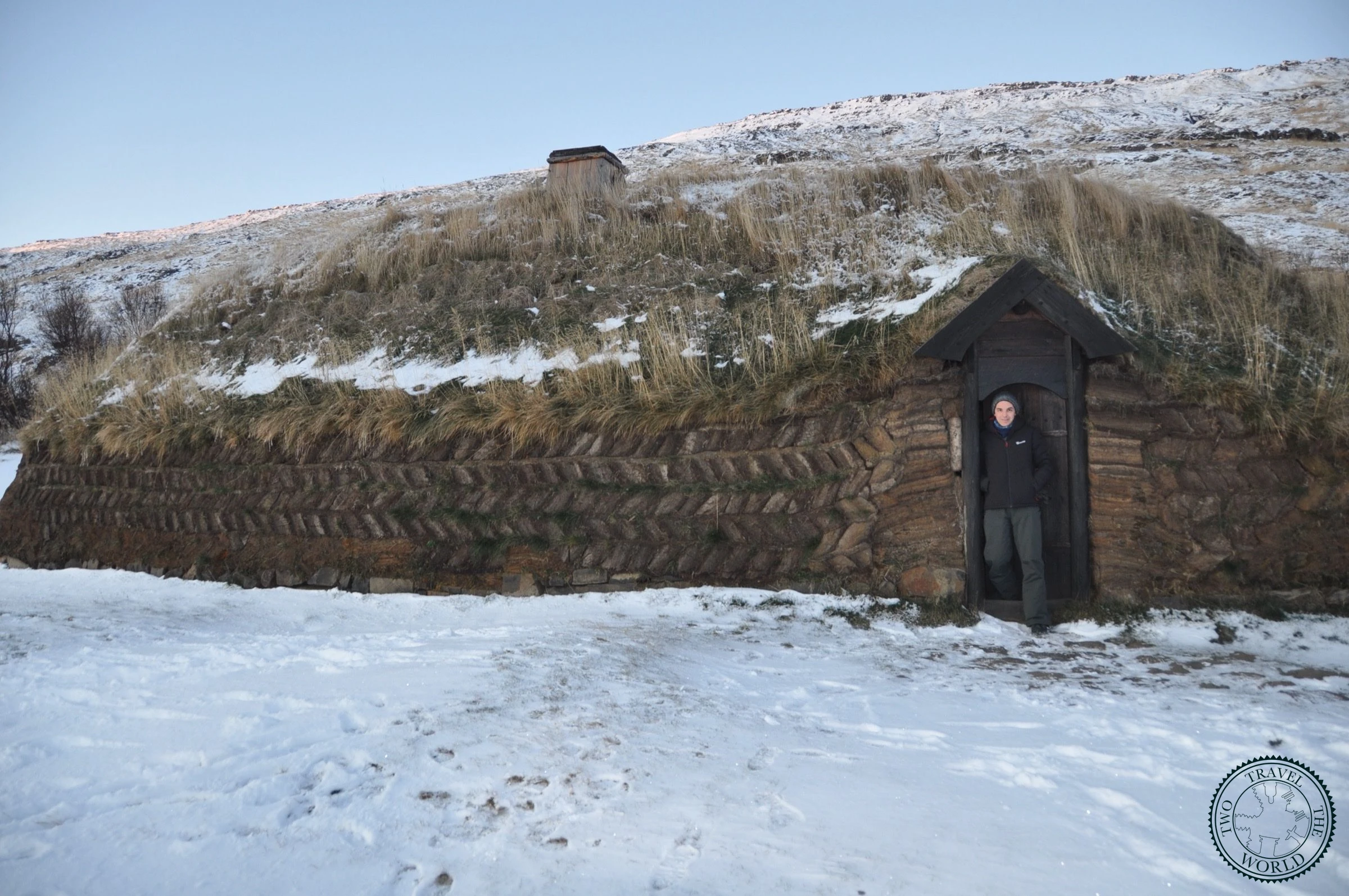 Visitor standing in the narrow doorway of the turf longhouse, showing the scale of the entrance